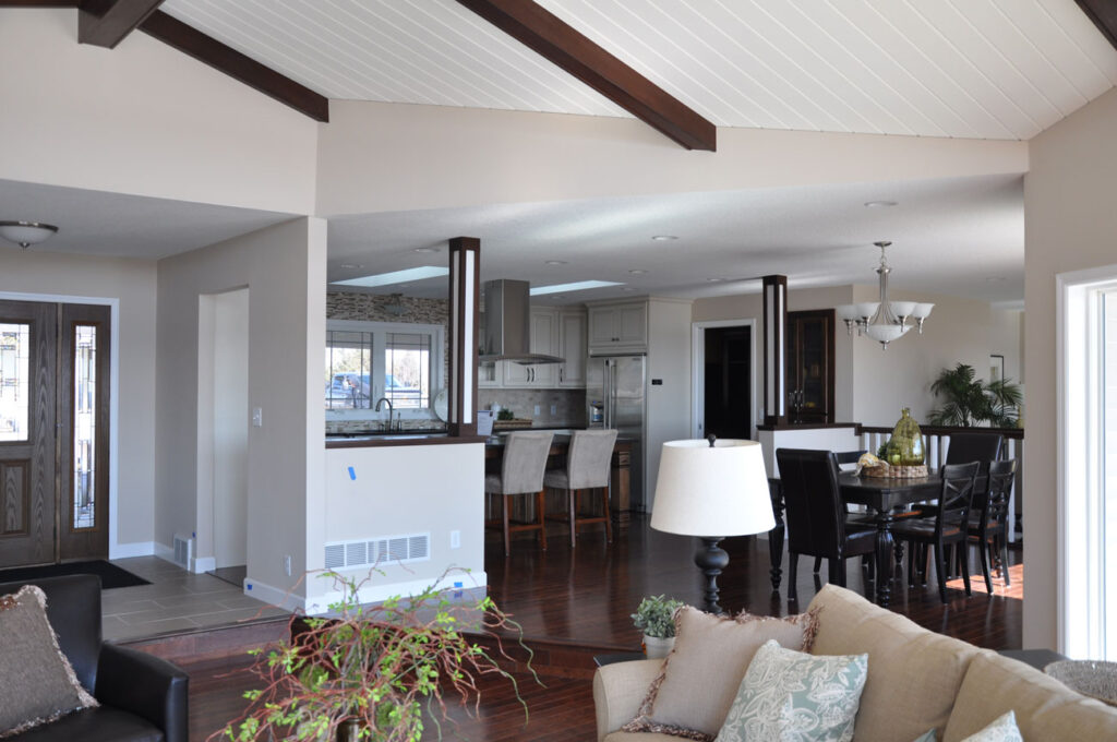 A modern open-concept living space with dark hardwood floors, exposed ceiling beams, and a view into the kitchen and dining area.