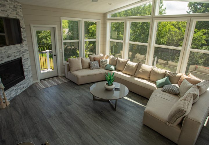 A serene enclosed patio featuring comfortable seating, a modern fireplace, and large windows that provide a view of the lush green surroundings.
