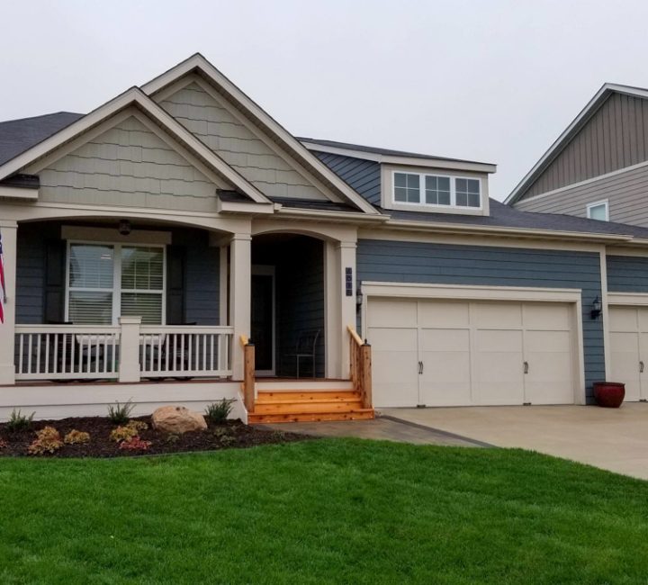 A charming home renovation featuring a new wooden front porch and a fresh exterior, complete with an American flag and landscaped garden.
