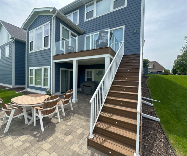 An elegant outdoor deck featuring a dining area with a wooden table set, complemented by a well-manicured lawn and modern house exterior.
