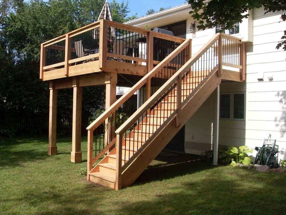 Stairs to the deck made of wood, and deck with chairs and unopened umbrella, and a grilling equipment