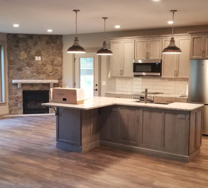 A remodeled kitchen with laminate floors, hanging lights, and built in cabinets