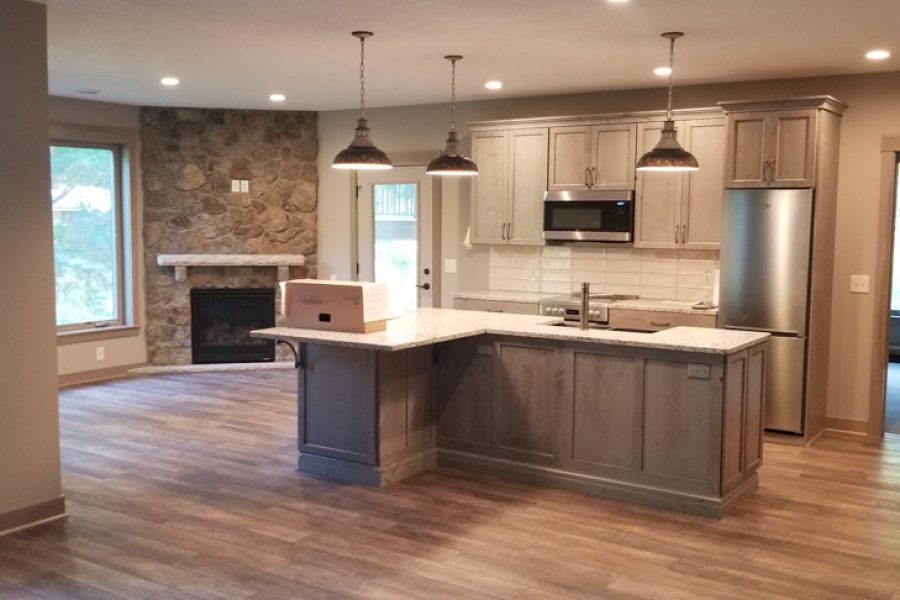 A remodeled kitchen with laminate floors, hanging lights, and built in cabinets