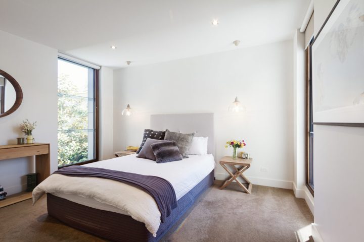 A bedroom with wide glass windows, carpeted floor and hanging lights on both sides of the bed