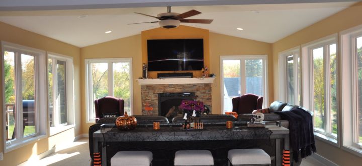 A living area for entertainment purposes, with a fireplace, wide sofa, a flat screen, and a ceiling fan