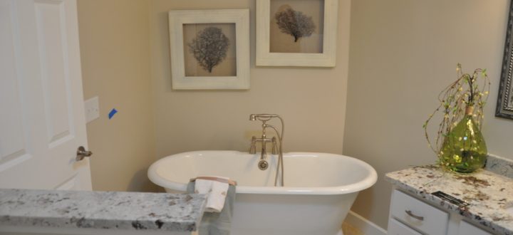 A freestanding bathtub in a bathroom, with art wall displays, marble countertops and white cabinets