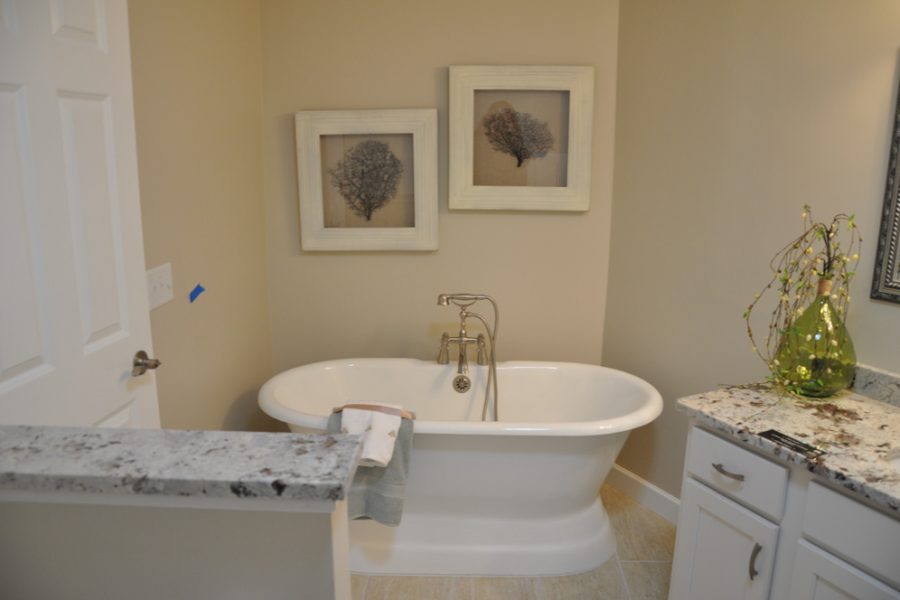 A freestanding bathtub in a bathroom, with art wall displays, marble countertops and white cabinets