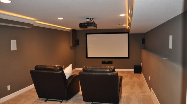 A home theater with carpeted floor, a projector, a white screen, and two cushioned chairs