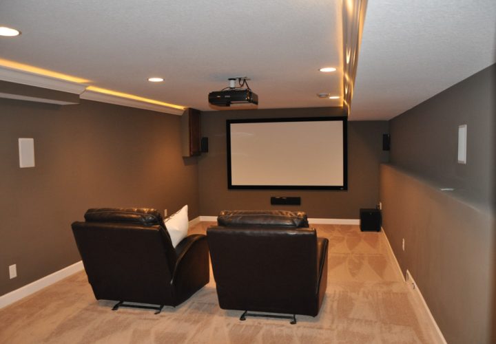 A home theater with carpeted floor, a projector, a white screen, and two cushioned chairs