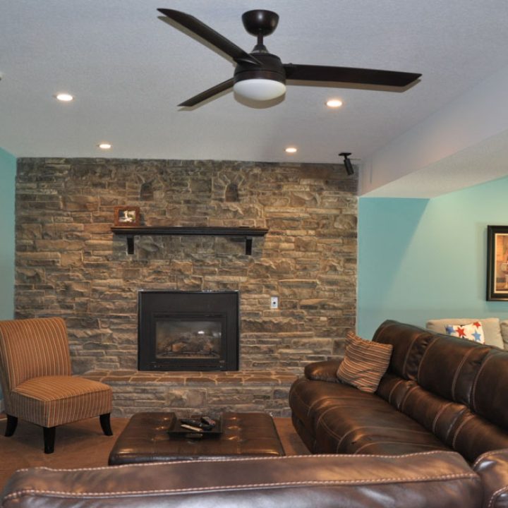 A living room with fireplace, leather cushioned couches, and a ceiling fan