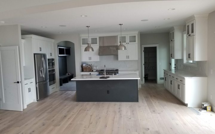 A wide kitchen with island, white cabinets built around appliances, and hanging light fixtures